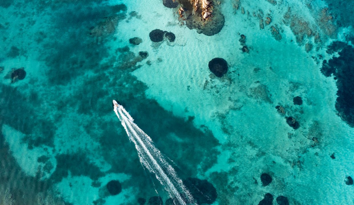 aerial boat navigating a turquoise sea waters in sardinia leaving a trail of its passage behind