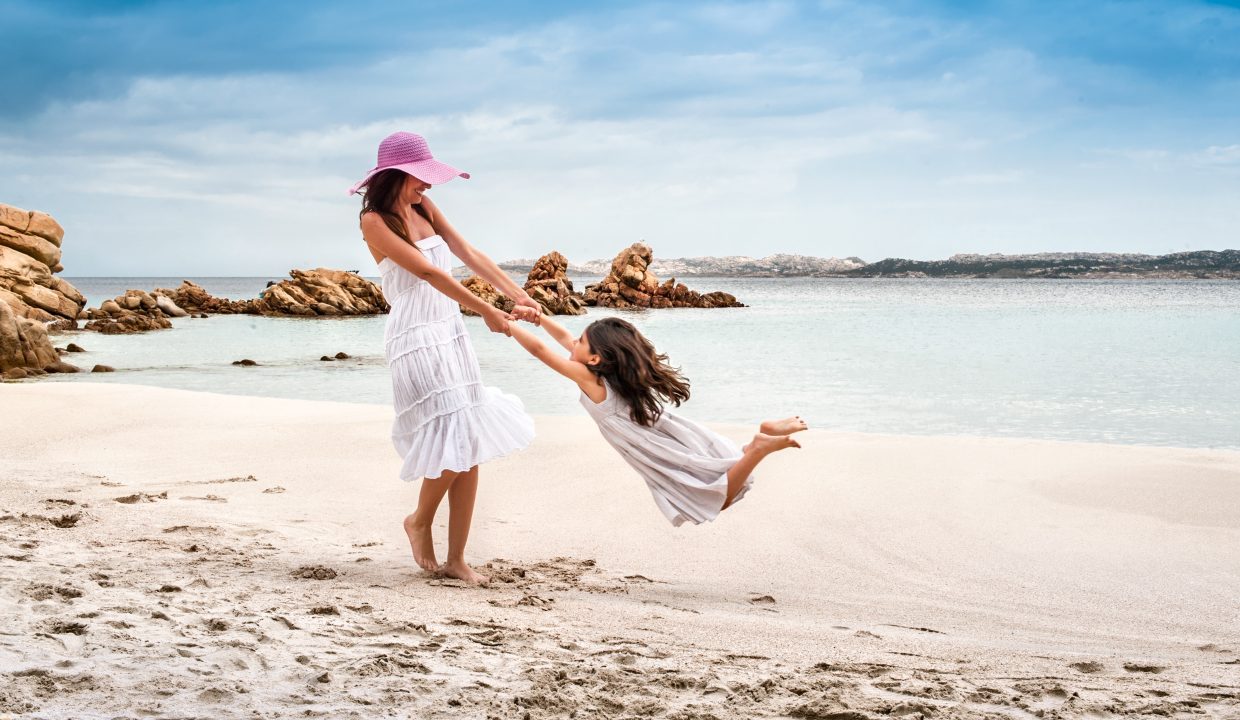 mother and daughter playing on a sardinia sandy beach with the sea on the background